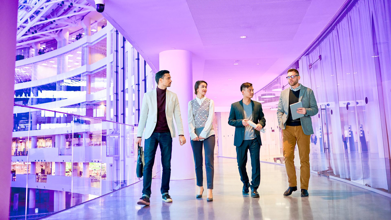 Group of professionals walking through a bright, modern office corridor with glass-panel architecture.