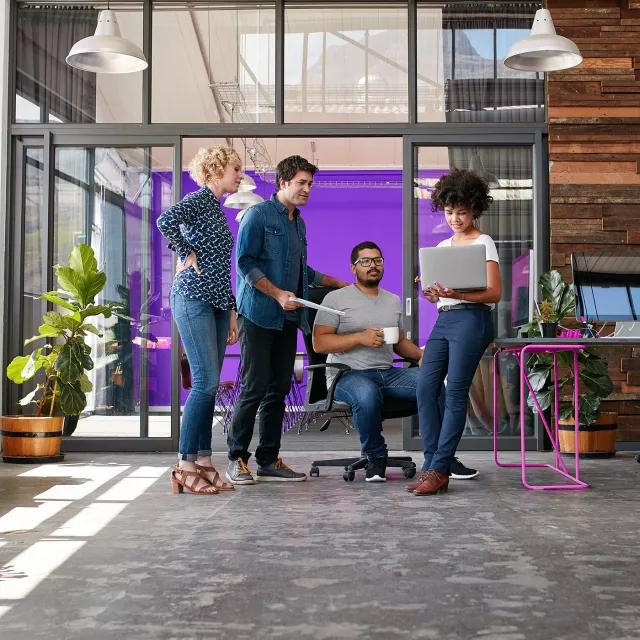 people in office gathered around laptop talking