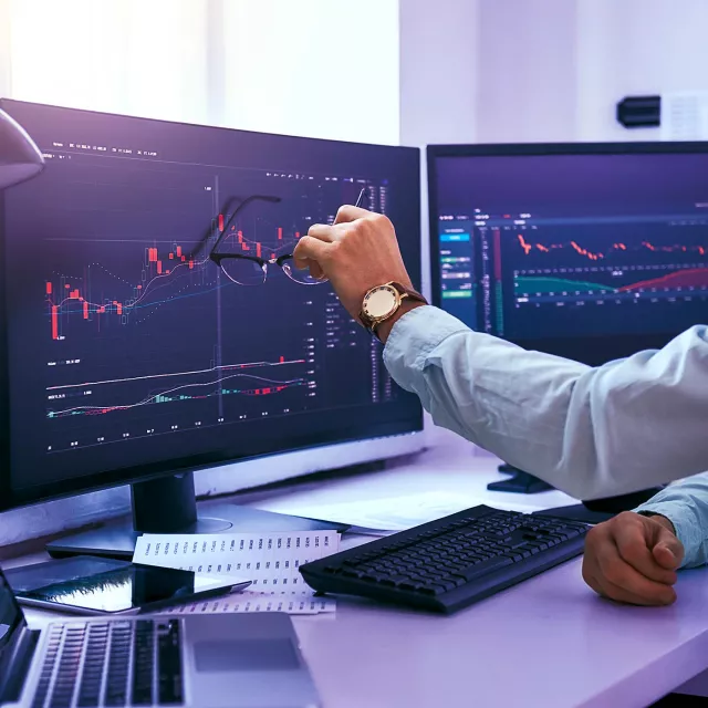 Image of hand holding eyeglasses in front of monitors