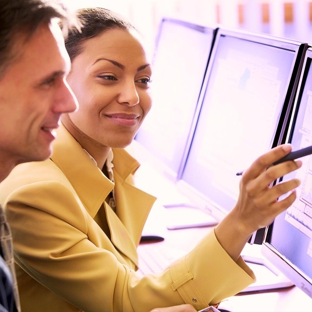 Image of woman pointing at monitor while man views monitor