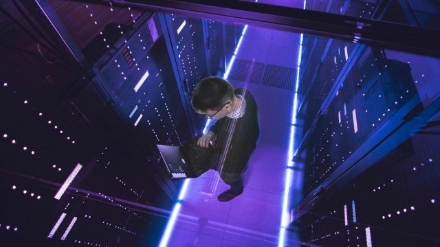 Image of a man in a servers room looking at his laptop