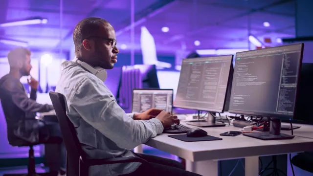 Image of man at the office, sitting at the desk and typing at the keyboard while looking at his two monitors