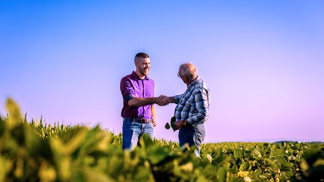 Image of young and old man shaking hands on a field