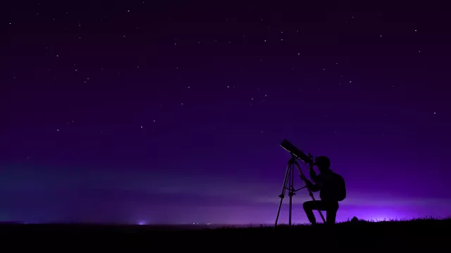 Image of person looking at the night sky through a telescope