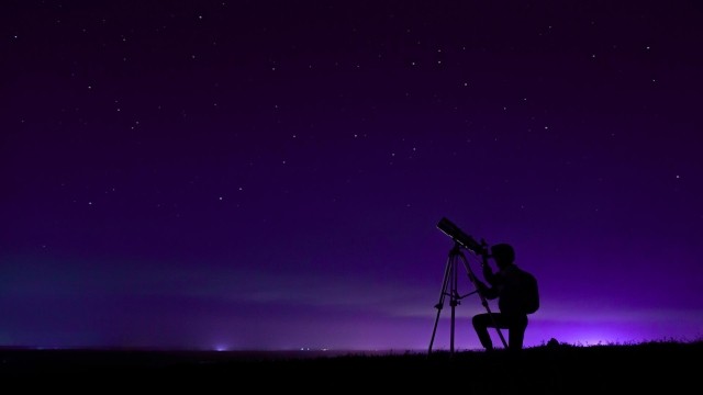 Image of man looking through a telescope outdoors at night