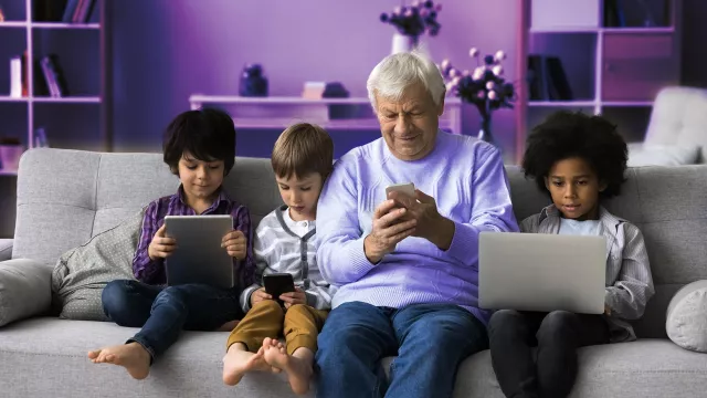 Image of elder man with 3 children sitting on the couch while looking at their devices