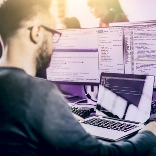 Image of man working on laptop with multiple monitors in the office
