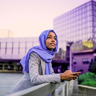 Image of woman holding mobile phone on a bridge looking up