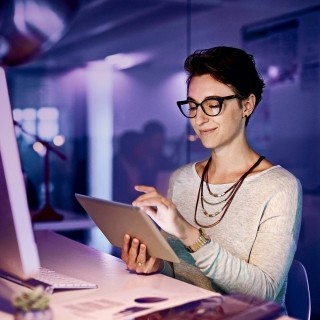 Image of woman working on tablet in front of a computer