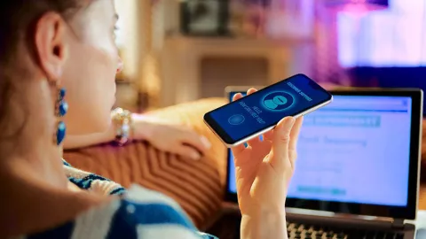 Image of woman calling on phone while working on a laptop at home