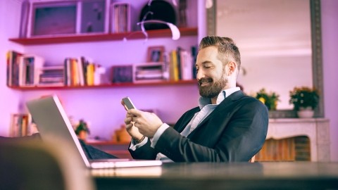 Image of a man smiling while looking at his phone sitting at the desk in his office