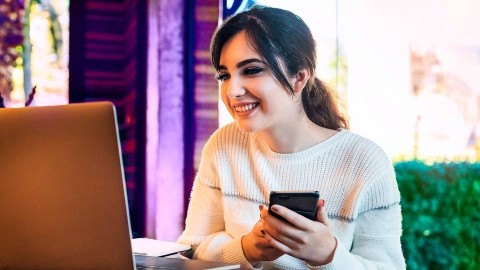 Image of woman looking at laptop while holding mobile phone