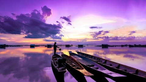 Image of man sitting on a boat next to three other boats on the lake at sunset